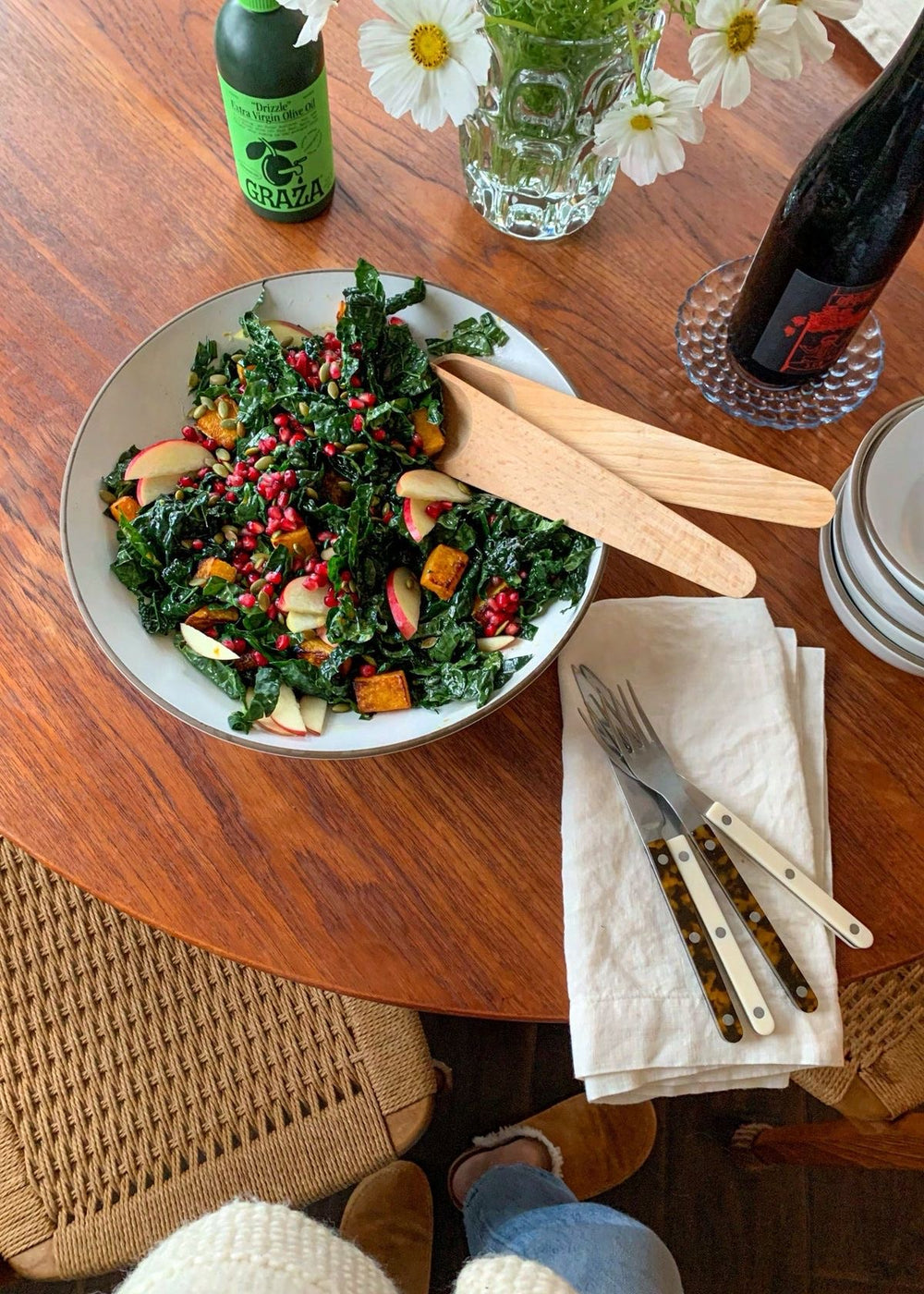 A salad on a wooden table next to a bottle of Graza
